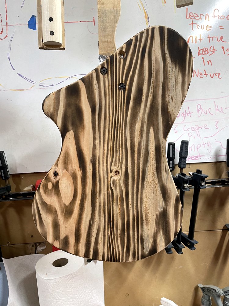 A guitar body with a scorched, high-contrast wood grain finish, clamped in the shop